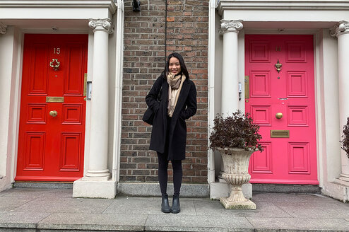 A person standing in front of two residential doors, one red and one pink